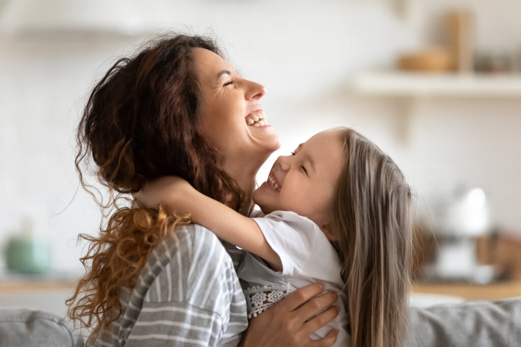 Mãe segurando filha nos braços, ambas sorridentes durante abraço.